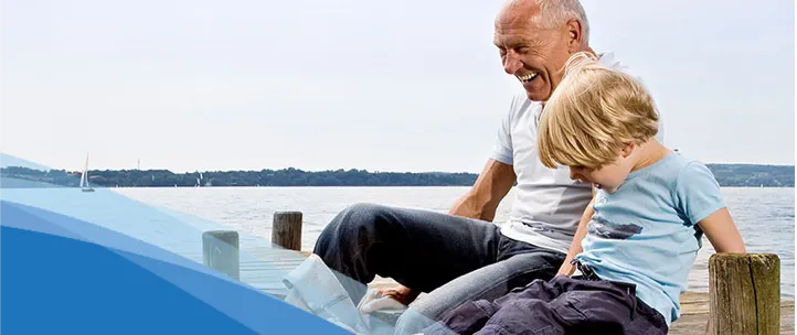 A grandfather and grandson sit on a dock. 